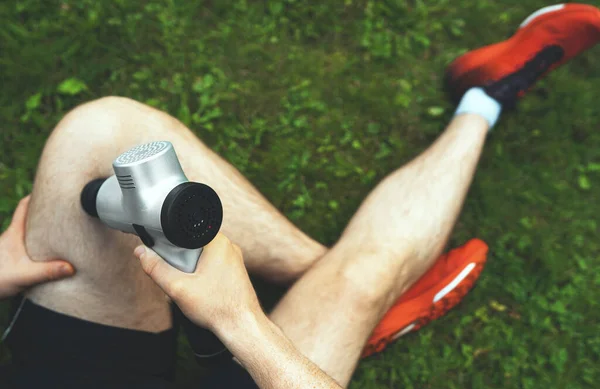 トレーニング後のマッサージ パーカッション デバイスで脚をマッサージする男 — ストック写真