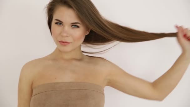 Hermosa chica rubia con hombros desnudos jugando con el pelo contra una pared blanca primer plano — Vídeo de stock