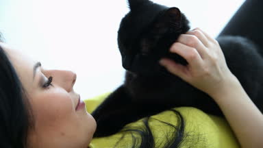 aşk için pets. siyah bir kedi ile güzel esmer kız evde oturma odasında kanepede rahatlatıcı.