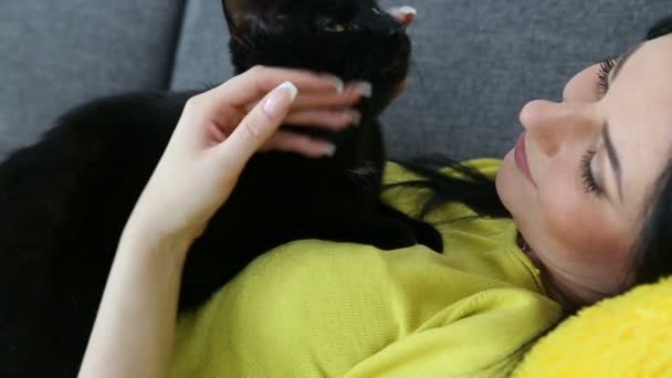 Kärlek för husdjur. vacker mörkhårig flicka med en svart katt är avkopplande hemma i vardagsrummet på soffan. — Stockvideo