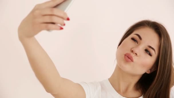 Moderne jeugd. mooie langharige meisje van Europees uiterlijk met bruin haar cancelbots praten op een smartphone videocommunicatie in de buurt van de witte muur — Stockvideo