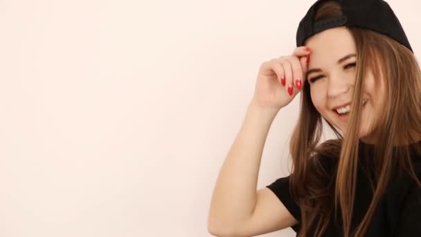 Teenage girl in trendy hip hop clothes and cap posing against white wall — Stock Video