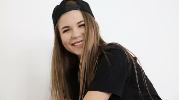 Teenage girl in trendy hip hop clothes and cap posing against white wall — Stock Video