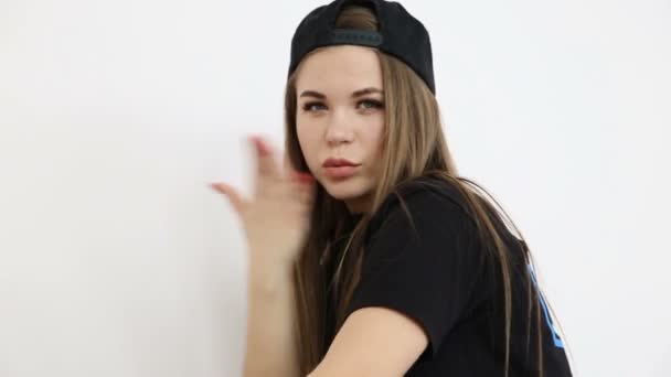 Teenager-Mädchen in trendiger Hip-Hop-Kleidung und Mütze posiert vor weißer Wand — Stockvideo