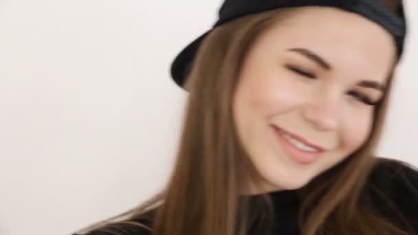 A teenage girl in black hip-hop clothes and a cap dances at the white wall- close-up, handheld shoot, small depth of field — Stock Video