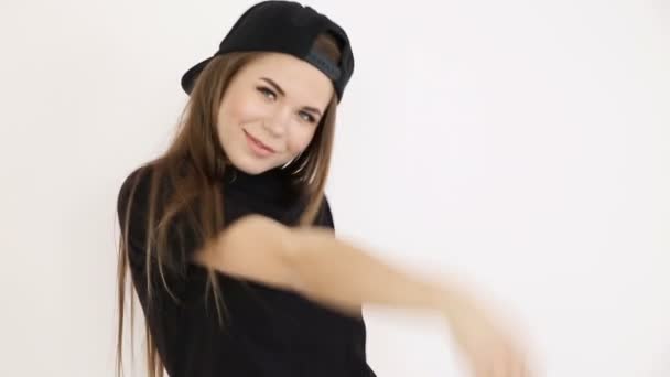 Девушка-подросток в черной хип-хоп одежде и кепке танцует на белой стене - крупный план, ручная съемка, малая глубина поля — стоковое видео