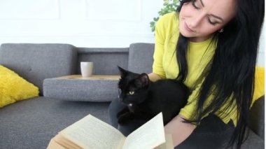 aşk için pets. siyah bir kedi ile güzel esmer kız evde oturma odasında kanepede rahatlatıcı.