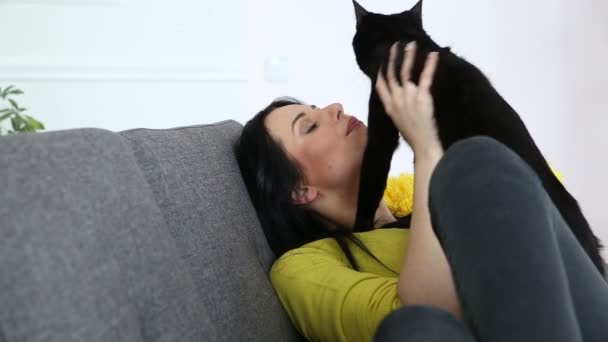 Liebe zu Haustieren. schöne dunkelhaarige Mädchen mit einer schwarzen Katze entspannt zu Hause im Wohnzimmer auf der Couch. — Stockvideo