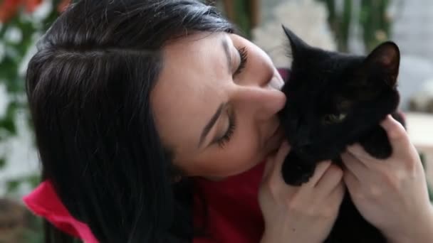 Amor por las mascotas. hermosa chica de pelo oscuro con un gato negro se relaja en casa en el dormitorio — Vídeo de stock