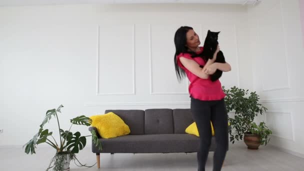 Любовь к домашним животным. красивая темноволосая девушка танцует с черной кошкой дома в гостиной — стоковое видео