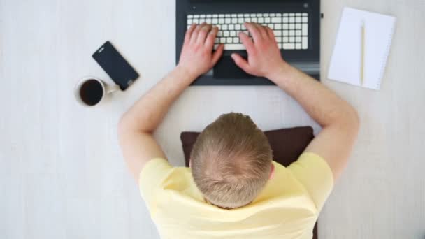 Un hombre independiente que trabaja en casa en el suelo detrás de un ordenador portátil — Vídeo de stock
