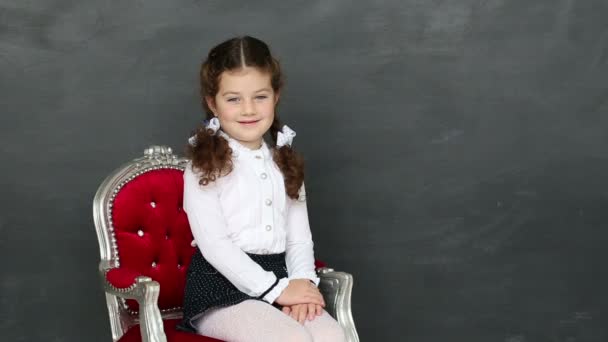 Menina sentada em uma cadeira perto de um conselho escolar — Vídeo de Stock