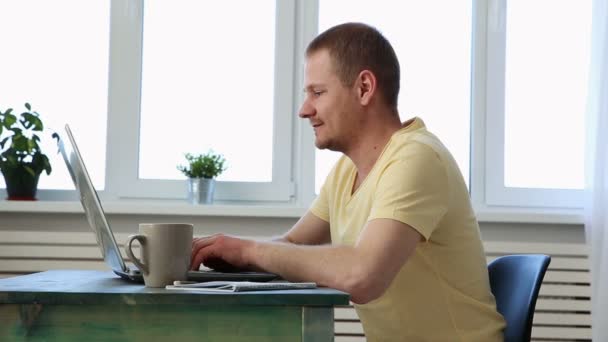 Успешный счастливый фрилансер работает дома за столом с ноутбуком и смотрит в камеру — стоковое видео