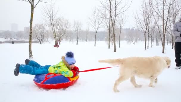 Família feliz com crianças e um cão se divertindo em um parque coberto de neve no inverno — Vídeo de Stock