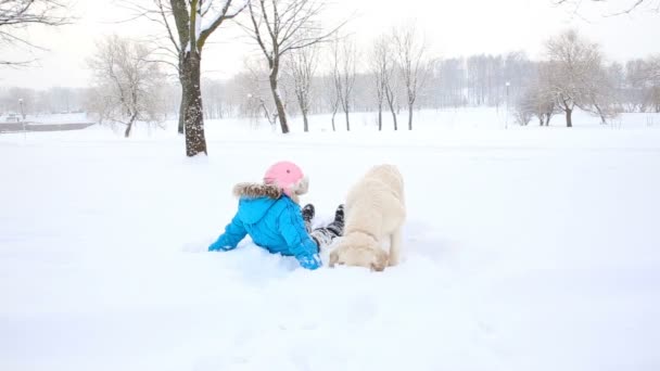 爱宠物-女孩在公园的雪中与一只金色的猎犬在休息 — 图库视频影像