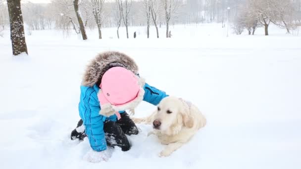 Amour pour les animaux de compagnie - la fille se repose avec un récupérateur d'or dans la neige dans le parc — Video
