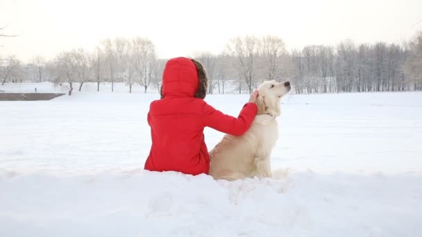 Miłość dla zwierząt - kobieta odpoczywa z golden retriever w śniegu w parku — Wideo stockowe