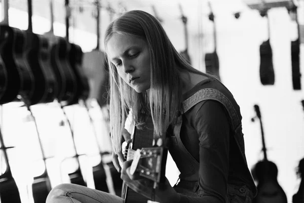 Foto de la calle al estilo de una vieja película en blanco y negro con grano - mujer moderna tocando una guitarra en una tienda de música — Foto de Stock