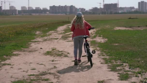 Hälsosam livsstil - tjej med en cykel som går på ett fält nära staden — Stockvideo