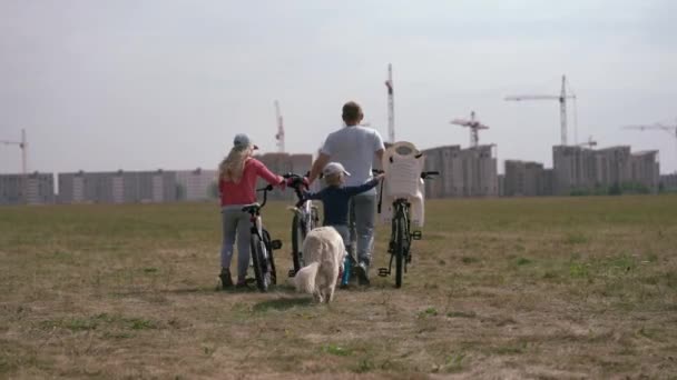 Stile di vita sano - famiglia con biciclette e un cane che cammina lungo il campo vicino alla città — Video Stock