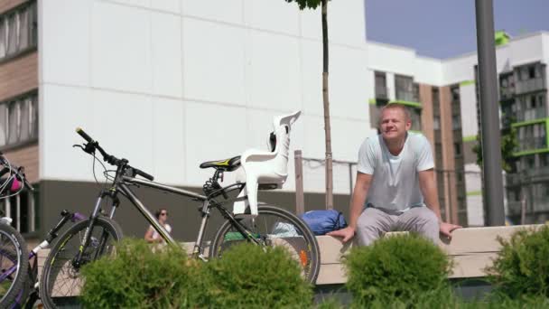 Moderní život ve velkém městě - sportovní mladý muž odpočívající na lavičce ve městě po jízda na kole — Stock video