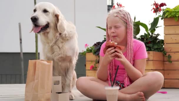 Kärlek för husdjur - vackra mode flicka med afrikanska flätor äter på gatan med sin hund — Stockvideo