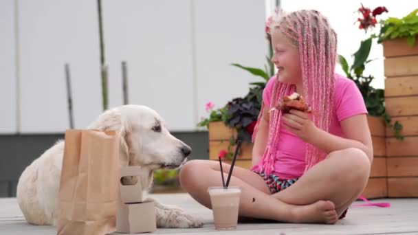 Amor por las mascotas - hermosa chica de moda con coletas africanas come en la calle con su perro — Vídeo de stock