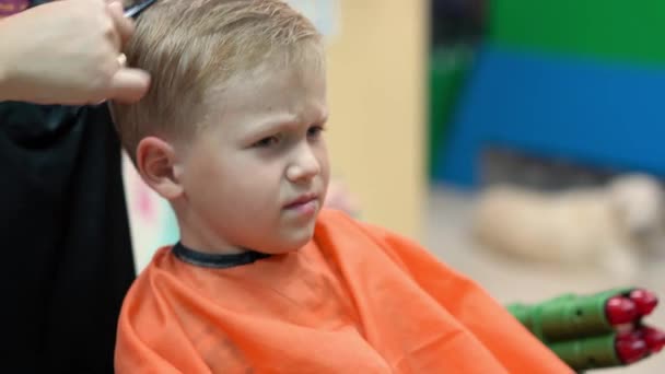 Стрижка маленького мальчика в детской парикмахерской — стоковое видео