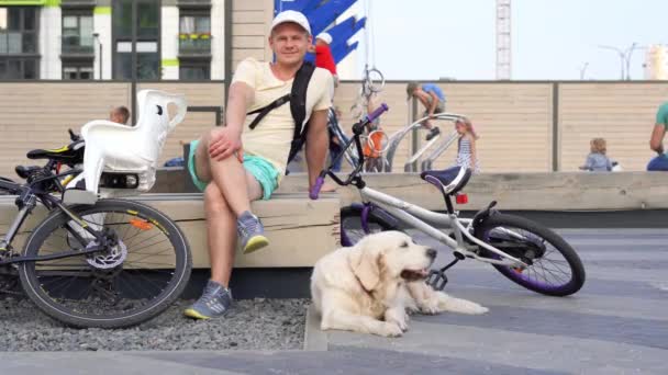 Moderna liv i en storstad - sportiga unga mannen med hunden vila på en bänk i staden efter en cykeltur — Stockvideo