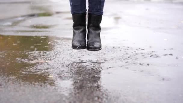 一个穿着黑色皮靴的女孩在雨中在秋天的水坑里跌跌撞撞 — 图库视频影像