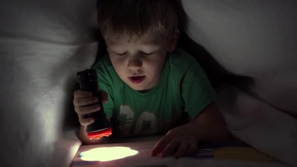 Niño leyendo un libro por la noche bajo una manta con una linterna — Vídeos de Stock