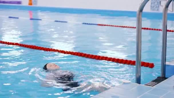 Уроки плавания для детей в бассейне - красивая светлокожая девочка плавает в воде — стоковое видео