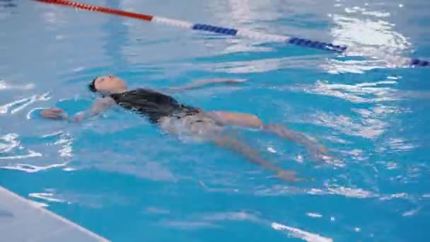 Clases de natación para niños en la piscina - hermosa chica de piel clara nada en el agua — Vídeo de stock