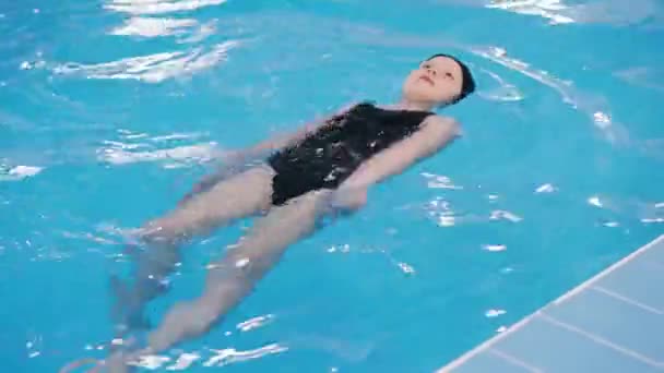 Уроки плавания для детей в бассейне - красивая светлокожая девочка плавает в воде — стоковое видео