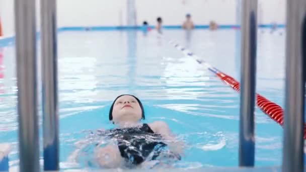 Lezioni di nuoto per bambini in piscina - bella ragazza dalla pelle chiara nuota in acqua — Video Stock