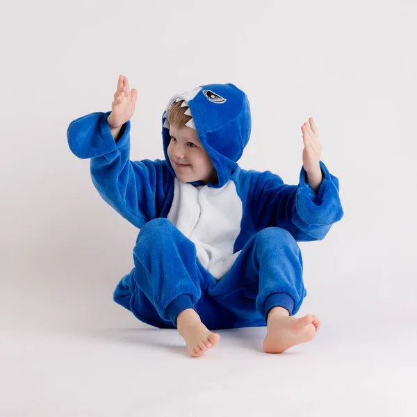 Menino alegre posando em um fundo branco em pijama, traje de tubarão azul — Fotografia de Stock