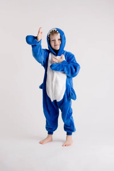 Menino alegre posando em um fundo branco em pijama, traje de tubarão azul — Fotografia de Stock