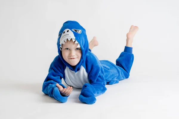 Niño alegre posando sobre un fondo blanco en pijama kigurumi, traje de tiburón azul — Foto de Stock