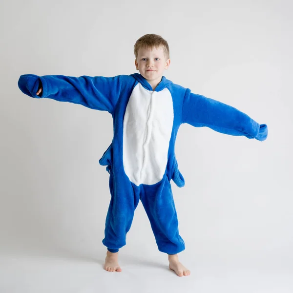 Menino alegre posando em um fundo branco em pijama, traje de tubarão azul — Fotografia de Stock