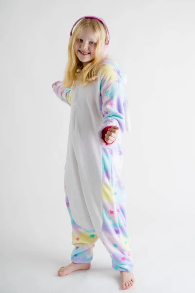 Modern divat - gyönyörű szőke lány hallgat zenét a fejhallgatót kigurumi pizsama fehér háttér Stock Kép