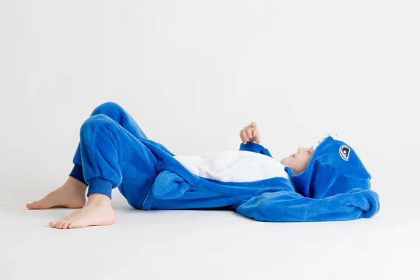 Menino alegre posando em um fundo branco em pijama, traje de tubarão azul — Fotografia de Stock