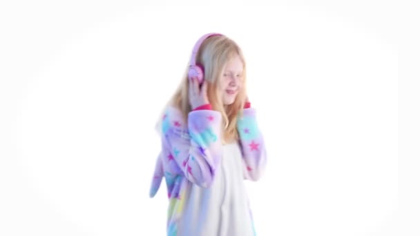 Modern divat - gyönyörű szőke lány hallgat zenét a fejhallgató és a tánc kigurumi pizsama - elszigetelt fehér fehér alapon — Stock videók