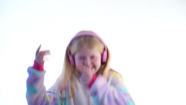 Moda moderna - bela menina loira escuta música com fones de ouvido e dança em um fundo branco em pijama kigurumi - isolado em branco — Vídeo de Stock