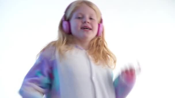 Mode moderne - belle fille blonde écoute de la musique avec écouteurs et danse sur un fond blanc en pyjama kigurumi - isolé sur blanc — Video