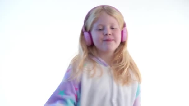 Moda moderna - hermosa chica rubia escucha música con auriculares y bailando sobre un fondo blanco en pijama kigurumi - aislado en blanco — Vídeos de Stock