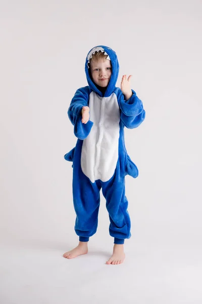 Menino alegre posando em um fundo branco em pijama, traje de tubarão azul — Fotografia de Stock