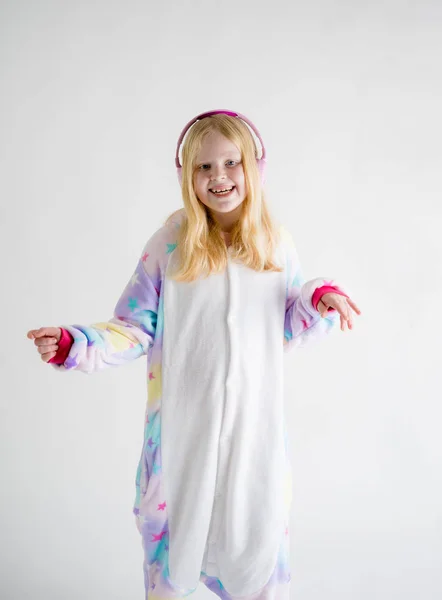モダンなファッション - 金髪美少女着ぐるみパジャマで白い背景の上にヘッドフォンで音楽を聴く — ストック写真