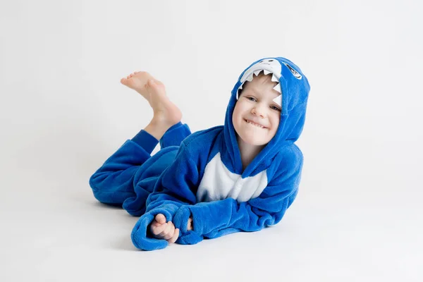 Niño alegre posando sobre un fondo blanco en pijama, traje de tiburón azul —  Fotos de Stock
