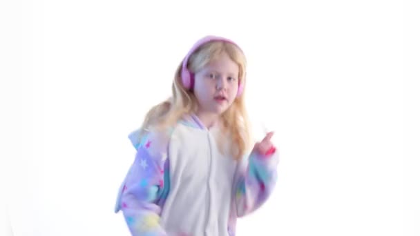 Современная мода - красивая блондинка слушает музыку с наушниками и танцует на белом фоне в пижаме кигуруми - изолированы на белом — стоковое видео