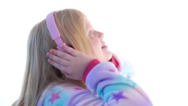 Moderní móda - krásná blond dívka poslouchá hudbu se sluchátky a tančí na bílém pozadí v kigurumi pyžama - izolované na bílém — Stock video